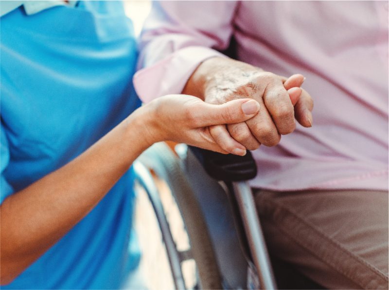 A nurse holds the hand of a wheelchair-bound older woman